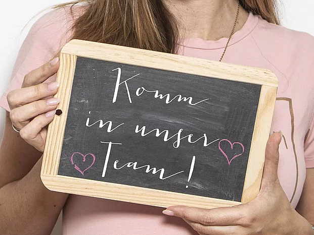Komm in unser Team Frau hält Schild hoch, mit dem Text: Komm in unser Team